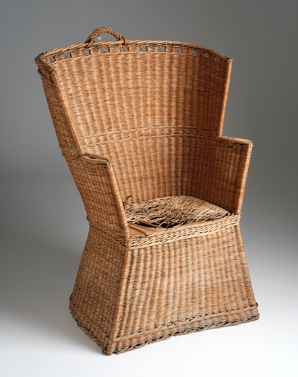 Nattstol fra Hans Nissengården laget av flettet tremateriale. Stolen har en pute av samme flettet materiale og et hull i setet for bruk som do. 