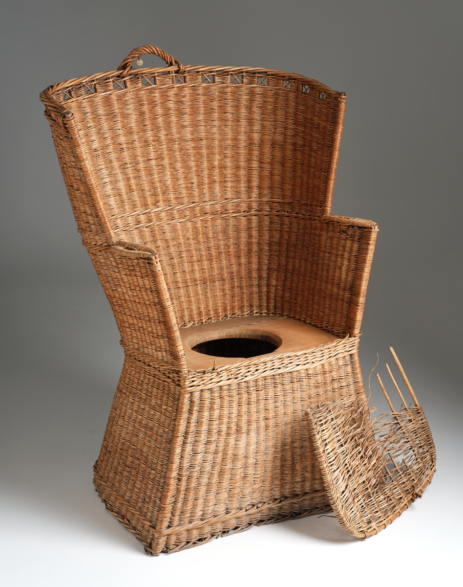 Nattstol fra Hans Nissengården laget av flettet tremateriale. Stolen har en pute av samme flettet materiale og et hull i setet for bruk som do. 
