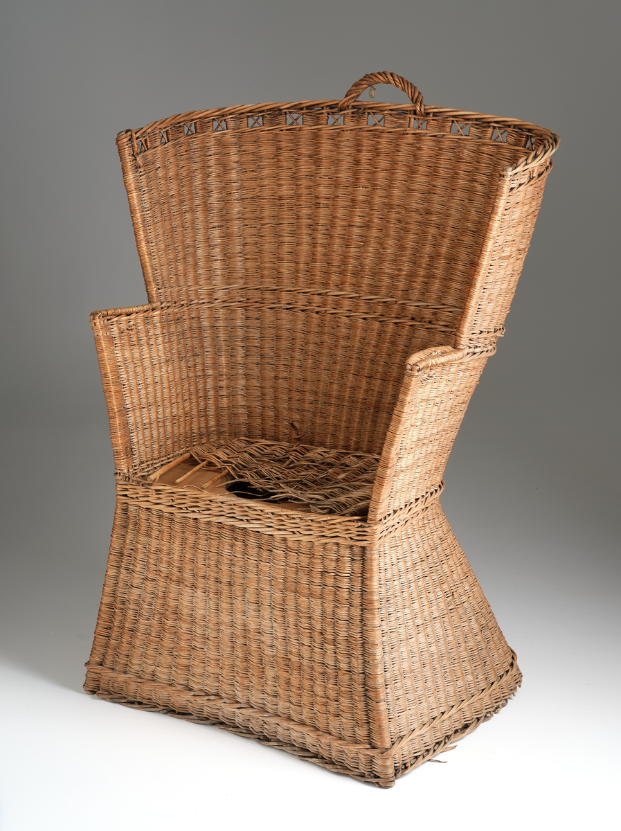 Nattstol fra Hans Nissengården laget av flettet tremateriale. Stolen har en pute av samme flettet materiale og et hull i setet for bruk som do. 