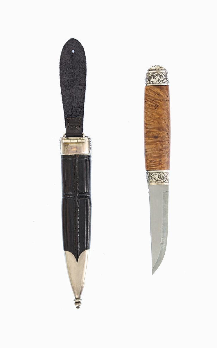 Staskniv frå knivmakar Øyvind Jeppesen.

Kniven har skaft truleg av valbjørk, med graverte sylvholkar og djevlemaske øvst.

Slire av lêr med pauta rankemønster. Slireholk og doppsko i gravert sylv.

Ranker på rutebotn i graveringane.