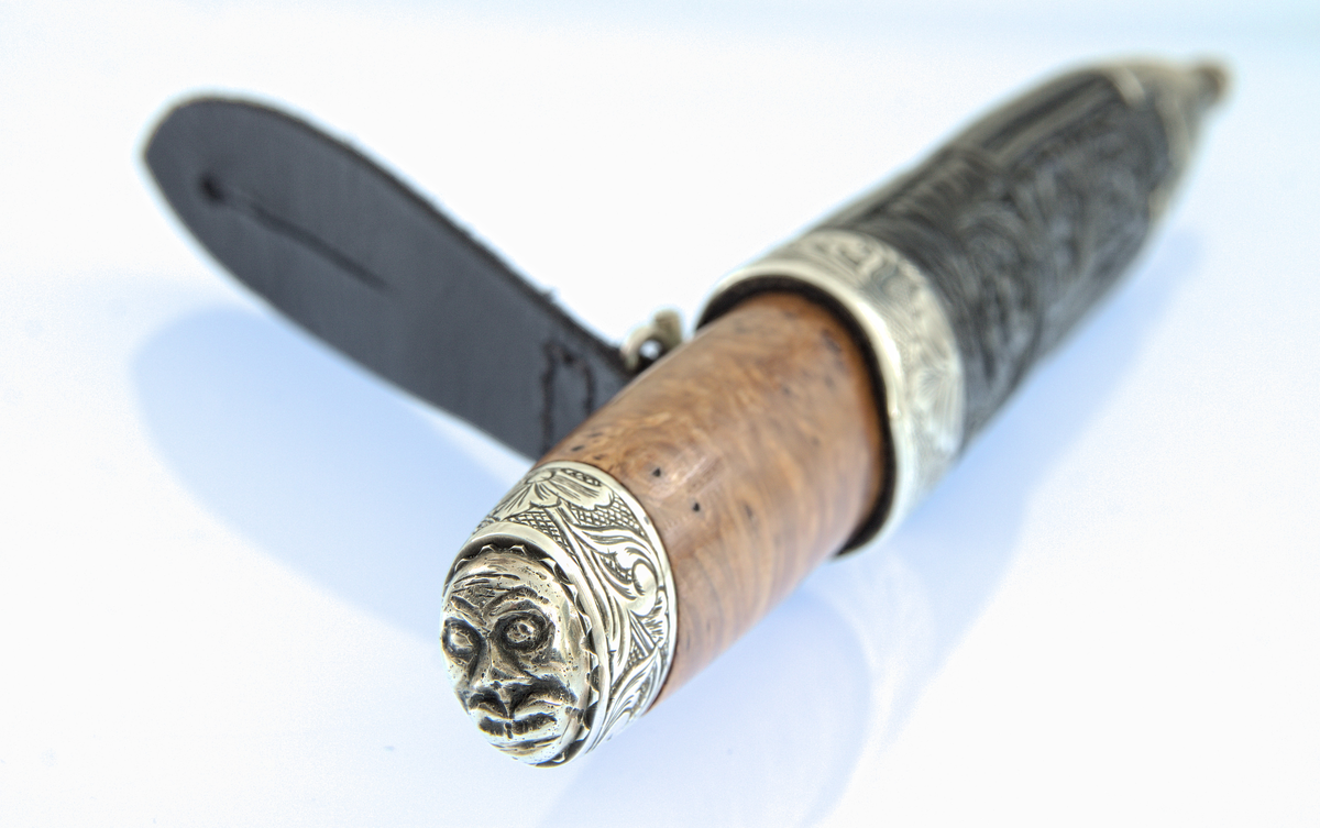 Staskniv frå knivmakar Øyvind Jeppesen.

Kniven har skaft truleg av valbjørk, med graverte sylvholkar og djevlemaske øvst.

Slire av lêr med pauta rankemønster. Slireholk og doppsko i gravert sylv.

Ranker på rutebotn i graveringane.