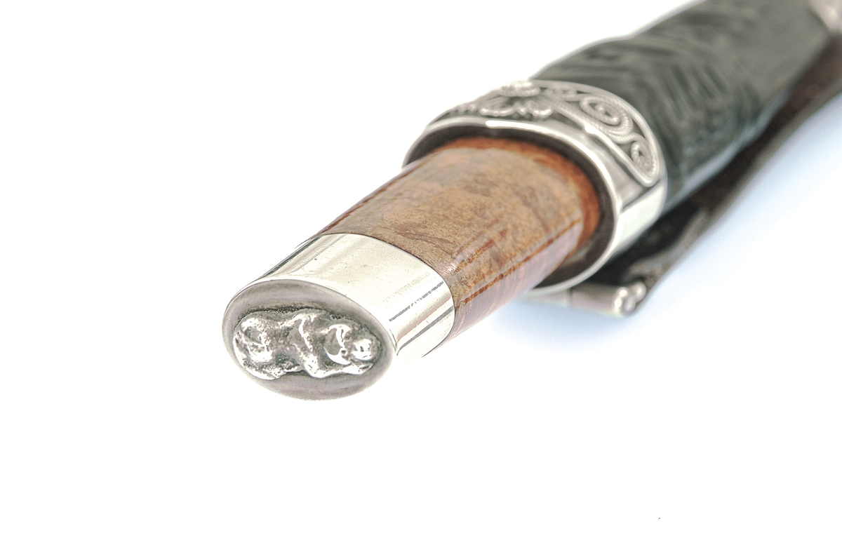 Staskniv frå knivmakar Hans Sjåberg.

Kniven ser ut til å ha skaft av bjørk, med enkle sylvholkar. Glibb forma som liggande bikkje.

Slira er av lêr og har pauta rankemønster. Holk og doppsko i sylv med filigranarbeid.
