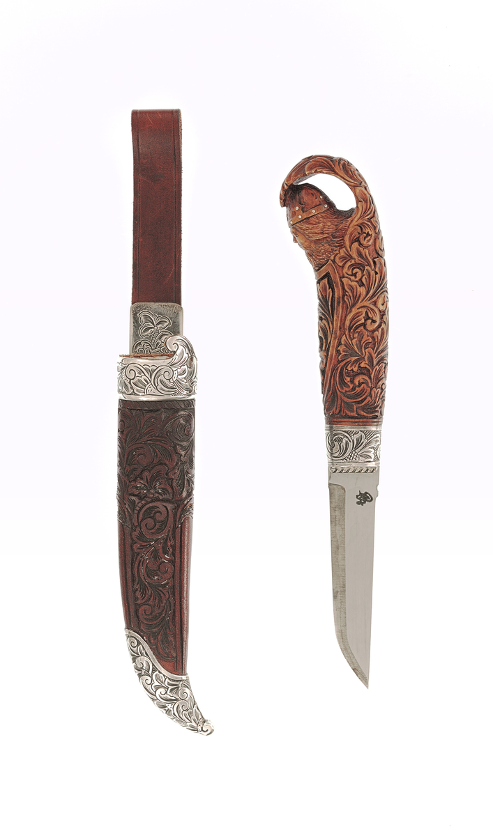 Staskniv frå knivmakar Rune Eriksen.

Kniven har skaft av tre utskore med olavshovud og rankeornamentikk. Holk i sylv nede, gravert med ranker på rutebotn.

Slira er av lêr med utskjeringar, her også rankemotiv. Slireholk, doppsko og innfesting i same utføring som knivholken. 
 
Krok.