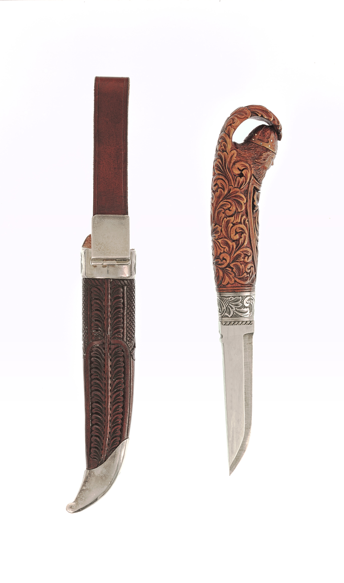 Staskniv frå knivmakar Rune Eriksen.

Kniven har skaft av tre utskore med olavshovud og rankeornamentikk. Holk i sylv nede, gravert med ranker på rutebotn.

Slira er av lêr med utskjeringar, her også rankemotiv. Slireholk, doppsko og innfesting i same utføring som knivholken. 
 
Krok.