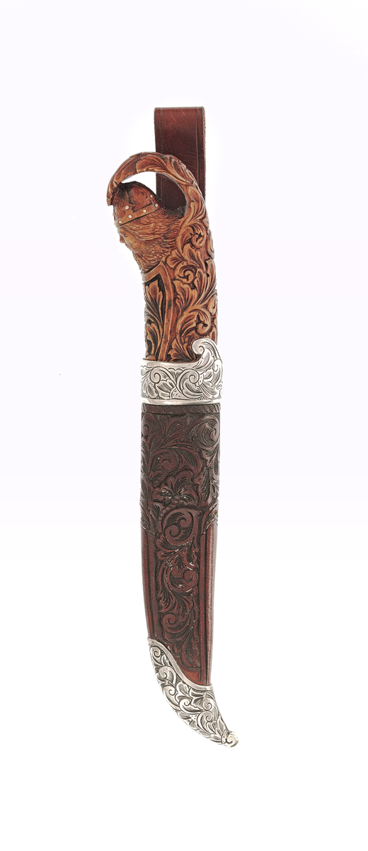 Staskniv frå knivmakar Rune Eriksen.

Kniven har skaft av tre utskore med olavshovud og rankeornamentikk. Holk i sylv nede, gravert med ranker på rutebotn.

Slira er av lêr med utskjeringar, her også rankemotiv. Slireholk, doppsko og innfesting i same utføring som knivholken. 
 
Krok.