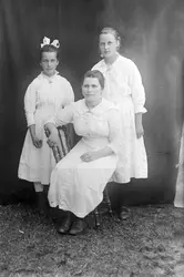 Portrett. Tre jenter. En jente sitter på en stol, to står. M