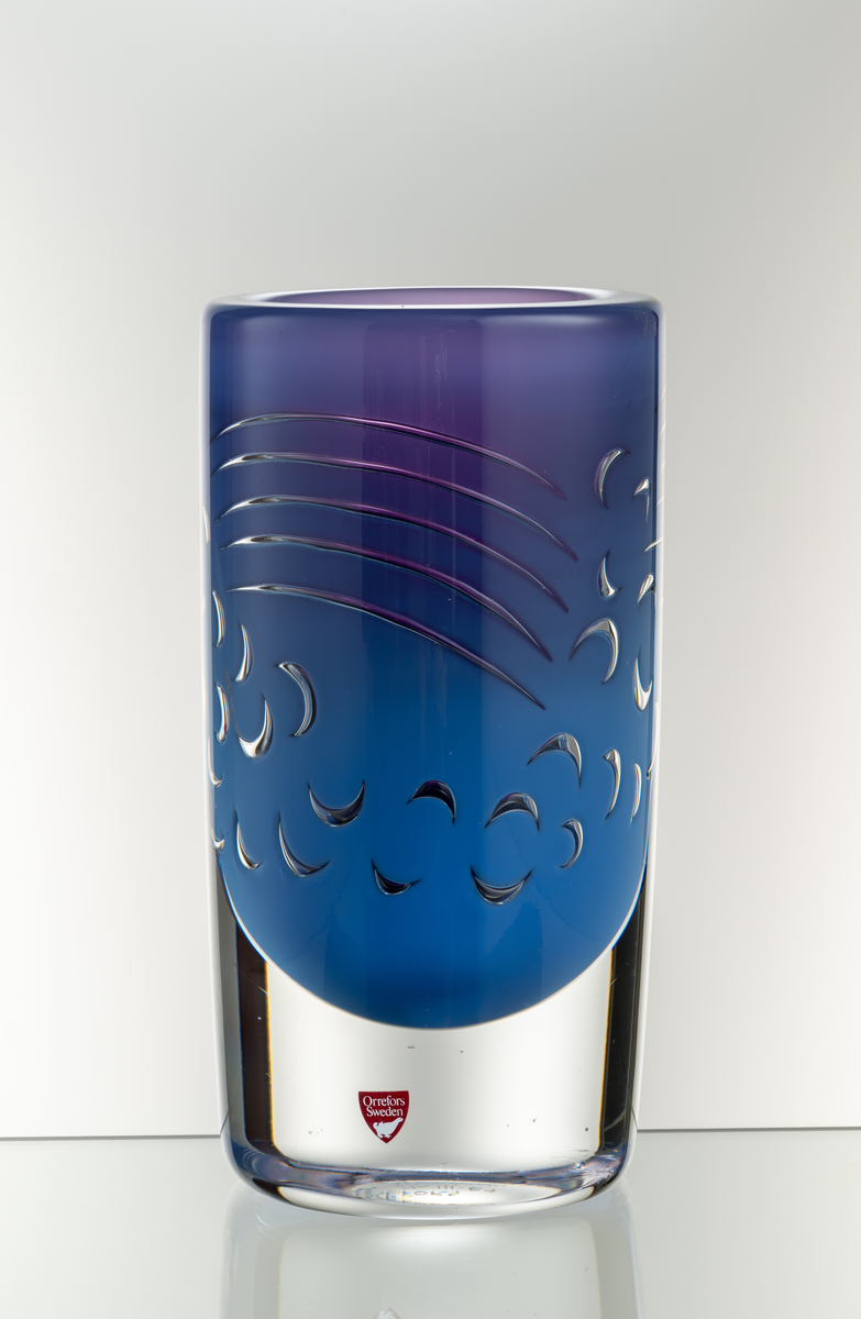 Arielvas, tjockväggig. Cylindrisk form. Ametistlila och delftblå färgton med abstrakt luftmönster i form av bågar och linjer.
Formgivare: Olle Alberius.