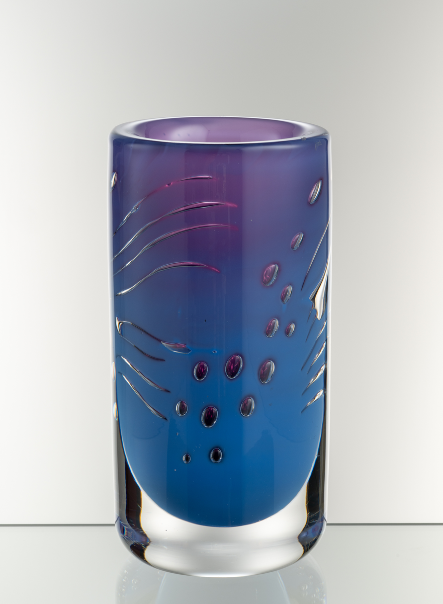 Arielvas, tjockväggig. Cylindrisk form. Ametistlila och delftblå färgton med abstrakt luftmönster i form av kulor och linjer.
Formgivare: Olle Alberius.