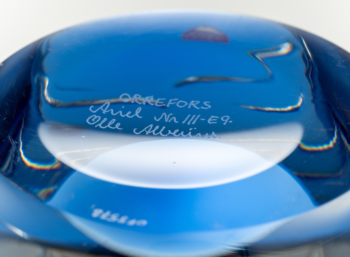 Arielvas, tjockväggig. Cylindrisk form. Ametistlila och delftblå färgton med abstrakt luftmönster i form av bågar och linjer.
Formgivare: Olle Alberius.