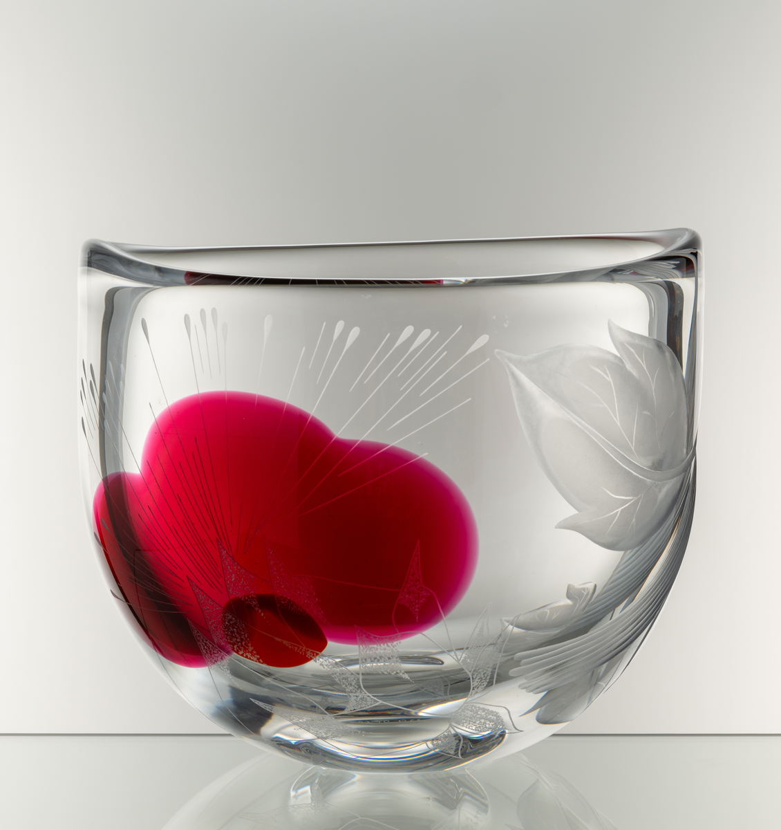 Skål, tjockväggig med oval form. Graverad dekor föreställande en trädform och en stor abstrakt blomma. Inlagda färgfält
i rött och orange.
Formgivare: Olle Alberius.