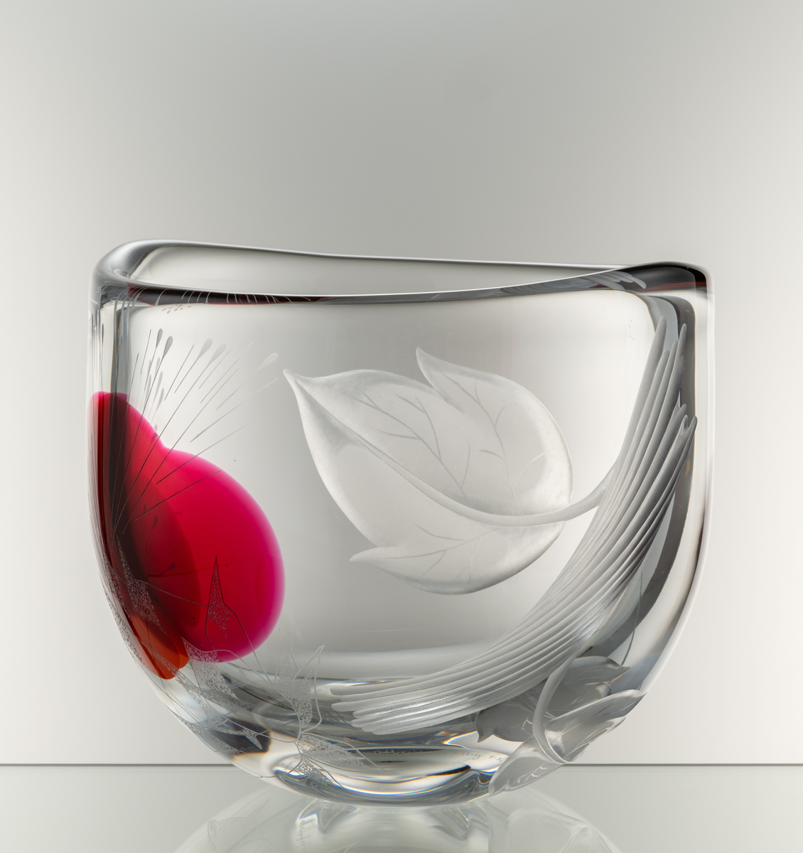 Skål, tjockväggig med oval form. Graverad dekor föreställande en trädform och en stor abstrakt blomma. Inlagda färgfält
i rött och orange.
Formgivare: Olle Alberius.