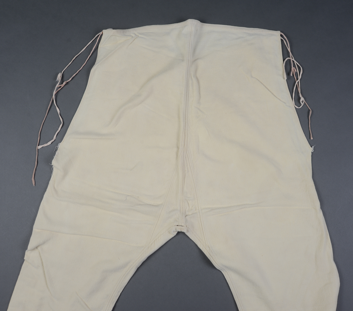 Hjemmesydd, knelang underbukse i gul/hvit flanell. Splitter i sidene, innsydd kile bakt. Bomullsbånd påsydd langs linningen, forlenget for knytting i livet. Buksa er ekstra høy i livet.