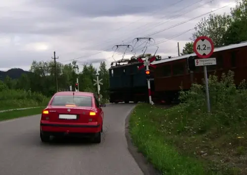 Rød bil foran planovergang med tog og blinkende rødt lys