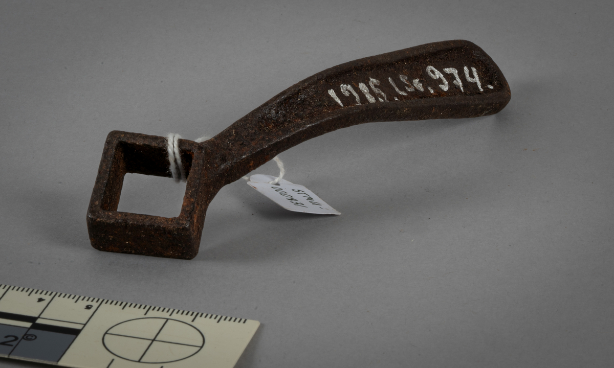 Skrunøkkel. Metall. 4-sidet øye i ene enden. Krumbøyd skaft med avrundet ende. Kantet på yttersidene.