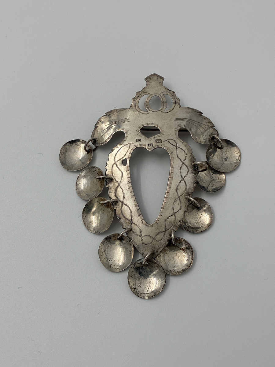 Hjärtformad bröstsölja med nio skålformade hängen.

Stadsstämpel: Hjorten= Alingsås
Årsstämpel: Y4= 1853
Mästarstämpel: AB= Anders Bäck