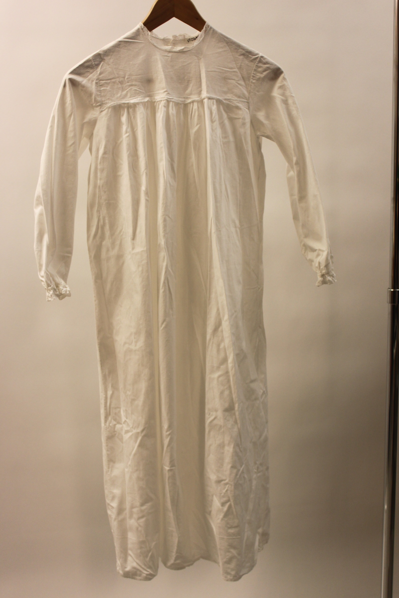 Lucialinne i barnstorlek. Maskinsydd med spetskantad halslinning och ärmslut. Även en spetskant längs nederkanten på oket. Kjolen rynkad mot oket. Knäpps med två vita knappar baktill.