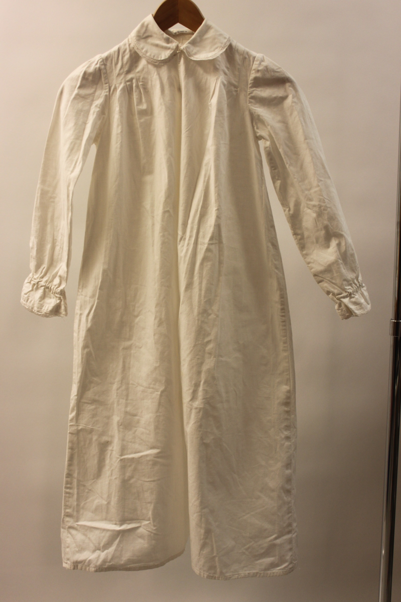 Lucialinne i bomullstyg. Barnstorlek. Hemsytt. försedd med vit spets i ärmslut och runt kragen. Sprund framtill som knäpps med en vit knapp. Tre lagda veck på bakstycket nedanför halslinningen och framtill på båda sidor om halslinningen.