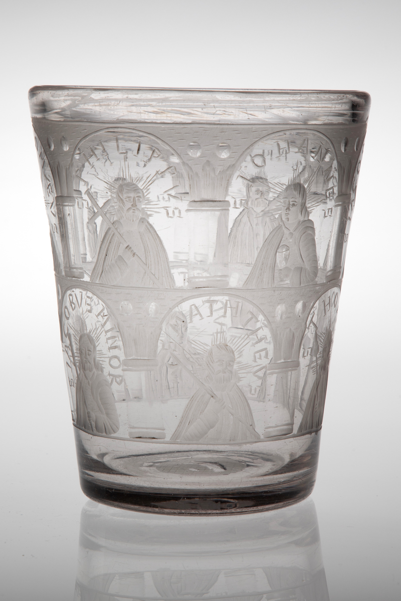 Tilnærmet sylinderformet beger i tykt klart glass med svakt koniske vegger. Yttersiden er dekorert med sliping og gravering, i form av arkadebuer i to etasjer som inndeler begerets overflate i tolv nisjer. I hver nisje er det fremstilt en av de tolv apostlene, som holder hver sitt ikonografiske attributt. Rester av puntemerke under bunnen. 

I øvre rekke:
1) Peter med nøkkel, omgitt av innskriften: "S P E T R V S".
2) Bartolomeus med sverd, omgitt av innskriften: "S B A R T H O L O M Æ V S".
3) Filip med kors, omgitt av innskriften: "S P H I L I P P V S".
4) Johannes med beger, omgitt av innskriften: "S I O H A N N E S".
5) Jakob den eldre med pilgrimsstav, omgitt av innskriften: "S I A C O B V S M A I O R".
6) Andreas med to diagonale planker på høyre side, antagelig en henvisning til det x-formede korset, omgitt av innskriften: "S A N D R E A S".

I nedre rekke: 
1) Matteus med hellebard, omgitt av innskriften: "S M A T H E V S".
2) Thomas med lanse, omgitt av innskriften: " S T H O M A S".
3) Mattias med øks, omgitt av innskriften: "S M A T H I A S".
4) Judas Taddeus med knortekjepp, omgitt av innskriften: "S I V D A S T H A DE V S".
5) Simon med sag, omgitt av innskriften: "S S I M O N I S"
6) Jakob den yngre med pilegrimsstav, omgitt av innskriften "S I A C O B V S M I N O R".