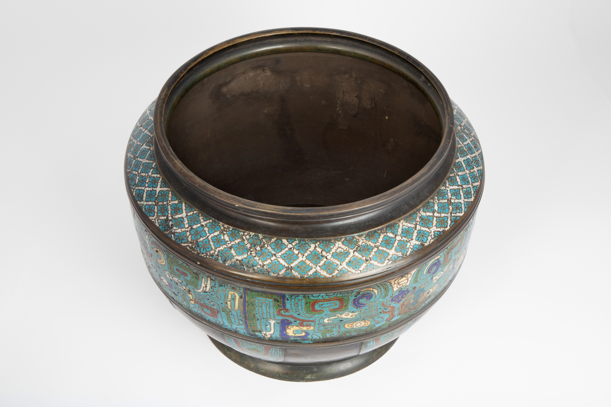 Kar i kobber, eventuelt en kobberlegering. Karet har en markert fotring som går over i en korpus med størst diameter omtrent midt på, før den trekker seg noe inn mot åpningen. Øverst avsluttes karet med en profilert munningskant. Rikt dekorert med et emaljert, polykromt mønster i cloisonné. På korpus et sammenhengende belte fylt med stiliserte, symmetriske ornamenter utført i turkist, grønt, hvitt, rødt og blått. Over dette et smalere belte med et repeterende geometrisk mønster i turkist og hvitt. Nederst på korpus felter med stiliserte, symmetriske ornamenter utført i turkist, grønt, hvitt, rødt og blått.