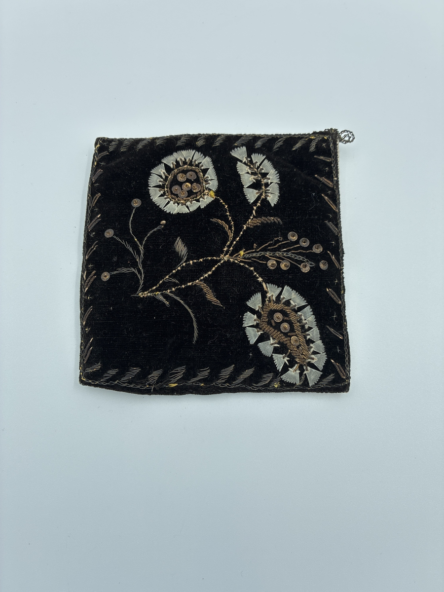 Fyrkantig dyna avsedd för placering av fickur.
Broderad och dekorerad med bl.a. fastsydda aborrfjäll.