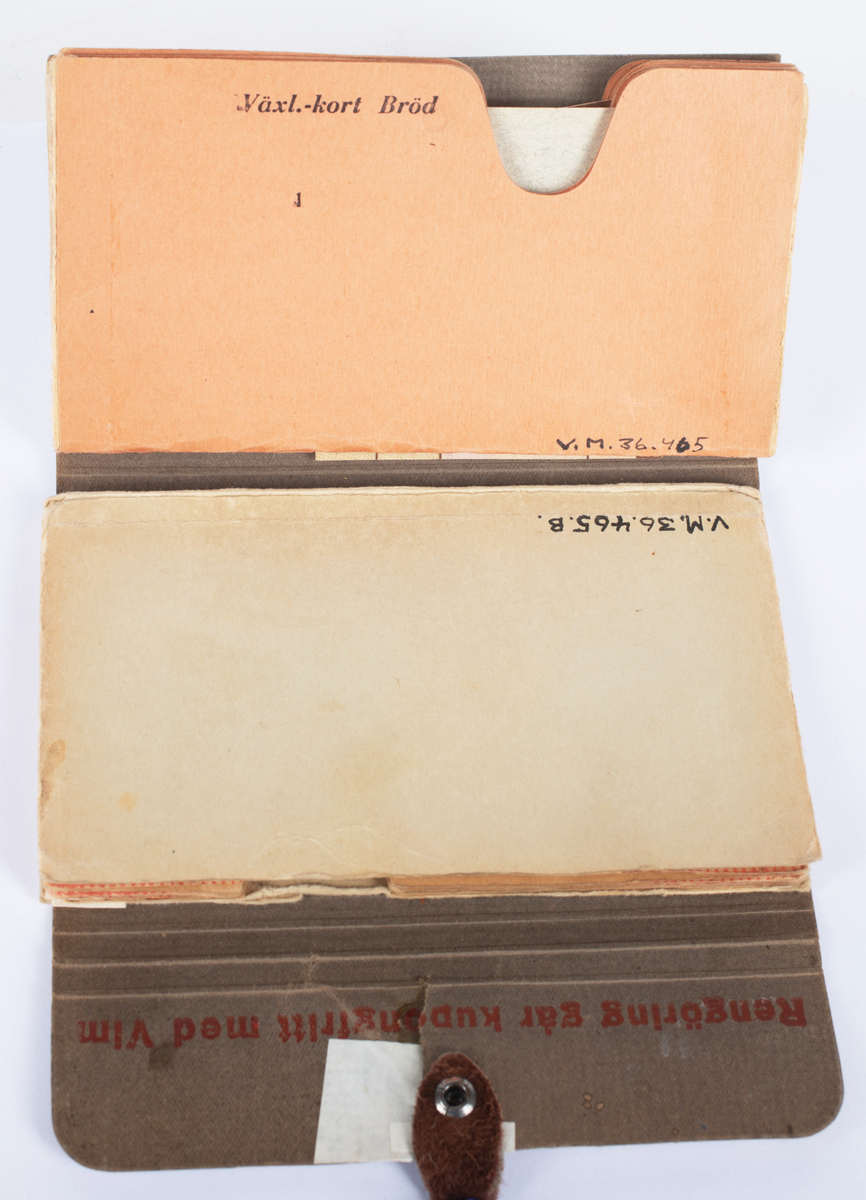 Portmonnä av papp, tryckknapp av järn och läderstropp. Använd till att förvara ransoneringskort i. Brun-gul melerad färg. Börsen har en mängd fack för de olika ransoneringskorten märkta "kaffe", "kött", "ägg", "kläder" m.m. Innehåller ransoneringskuponger av olika slag.