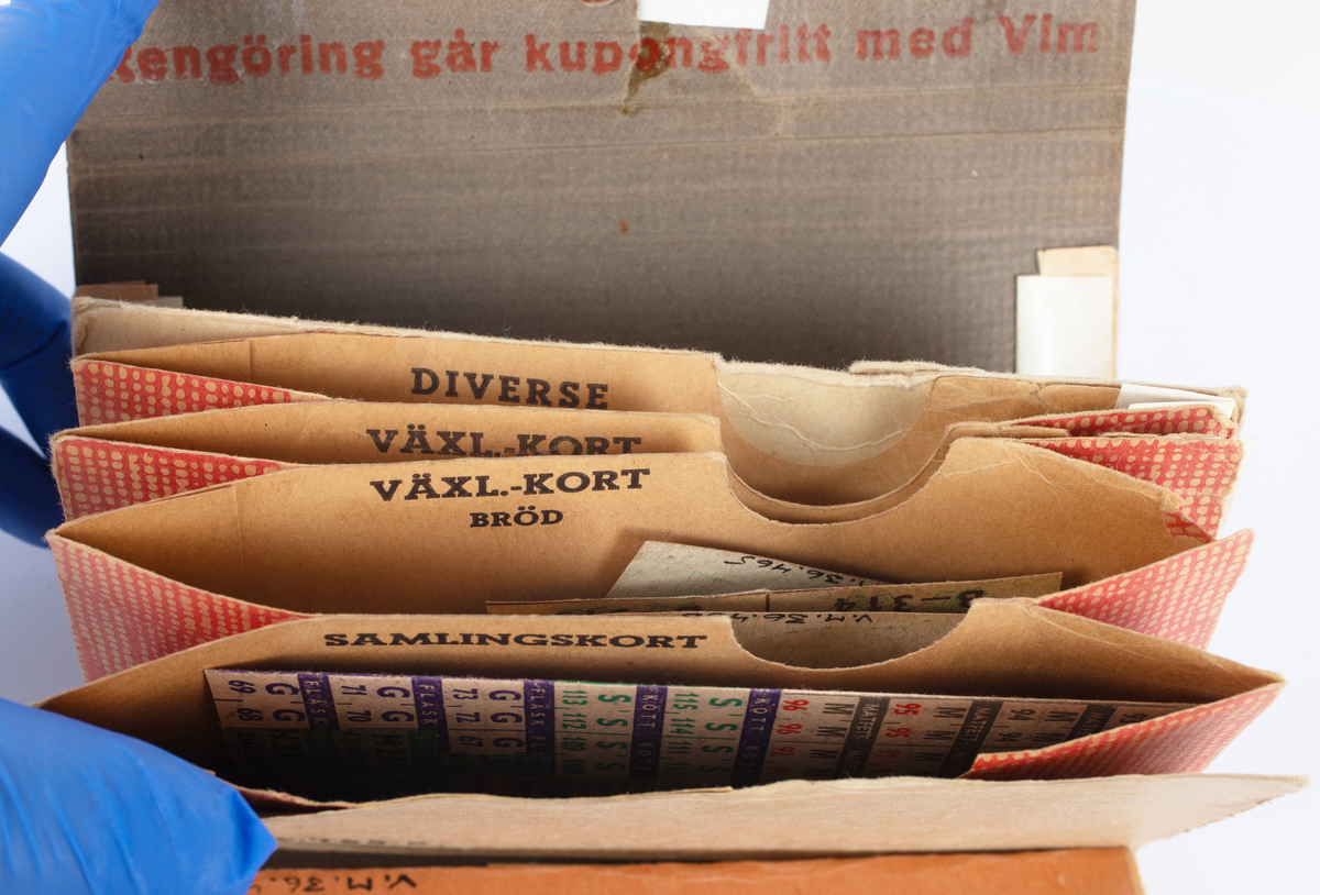 Portmonnä av papp, tryckknapp av järn och läderstropp. Använd till att förvara ransoneringskort i. Brun-gul melerad färg. Börsen har en mängd fack för de olika ransoneringskorten märkta "kaffe", "kött", "ägg", "kläder" m.m. Innehåller ransoneringskuponger av olika slag.