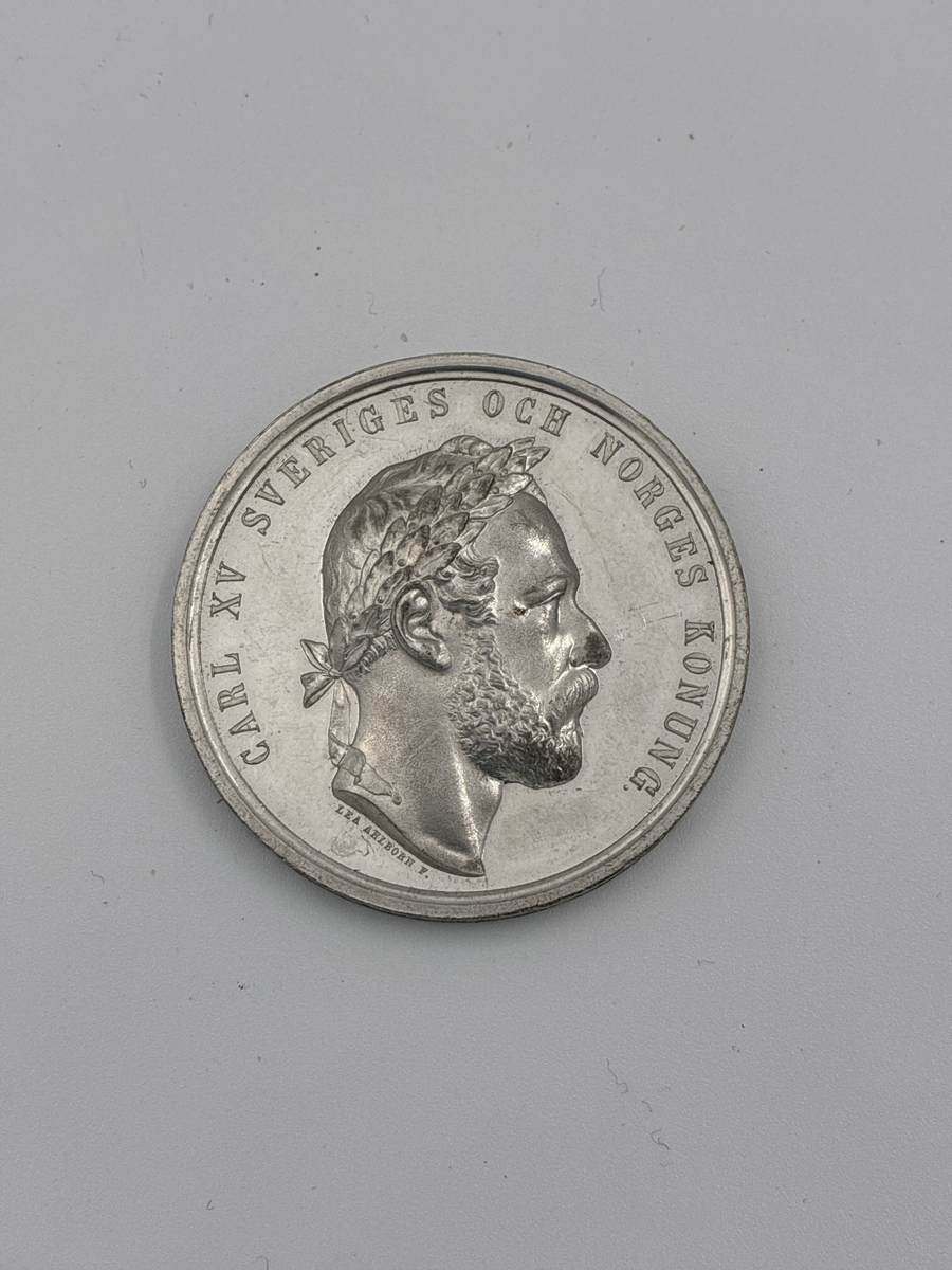 Minnesmedalj över Carl XV dödsdag. 

På ena sidan "Carl XV Sveriges och Norges konung" samt porträtt i profil. 
Andra sidan "Fredsäll  Folkkär" med sittande kvinna (moder Svea?) som håller en skylt med texten "Den 18 sept 1872"

Myntet är signerat Lea Ahlborn som var statiligt anställd som mynt- och medaljgravör 1855-1897.