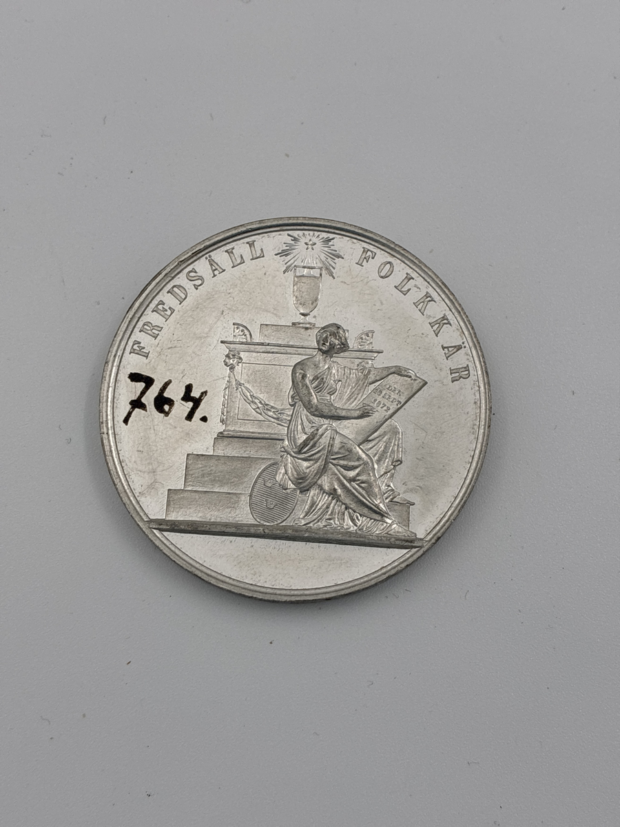 Minnesmedalj över Carl XV dödsdag. 

På ena sidan "Carl XV Sveriges och Norges konung" samt porträtt i profil. 
Andra sidan "Fredsäll  Folkkär" med sittande kvinna (moder Svea?) som håller en skylt med texten "Den 18 sept 1872"

Myntet är signerat Lea Ahlborn som var statiligt anställd som mynt- och medaljgravör 1855-1897.