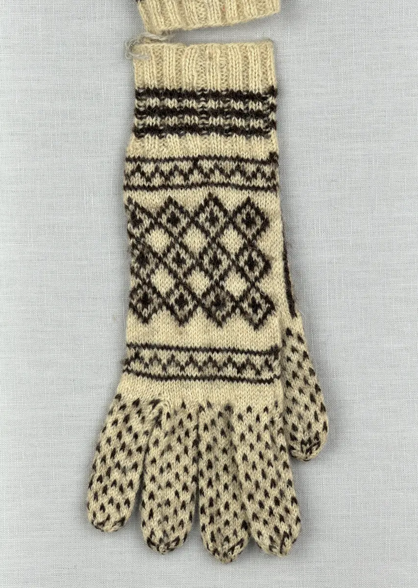 Ett par stickade fingervantar, med randig mudd i 2-2 resår (2 räta och 2 aviga maskor) och mönsterstickad vante i slätstickning, av 2-trådigt ullgarn.
