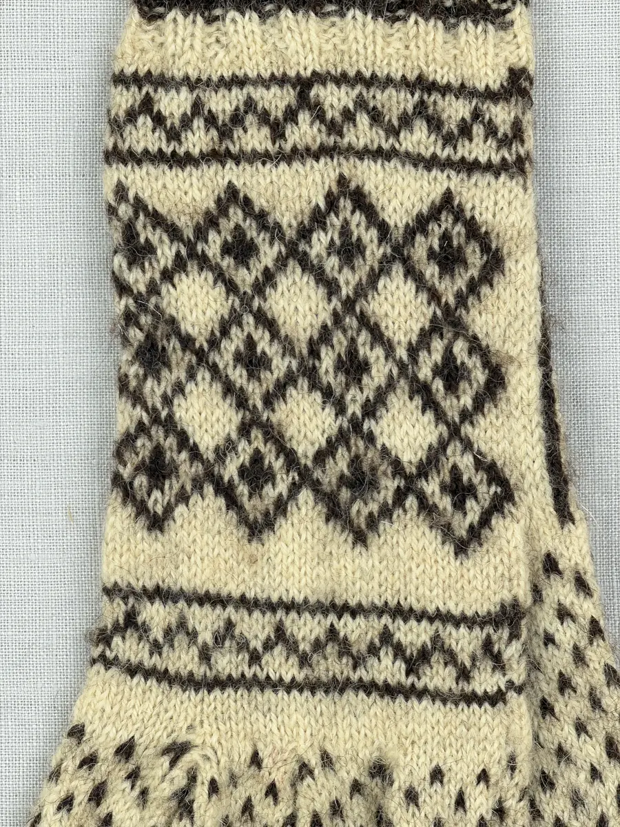 Ett par stickade fingervantar, med randig mudd i 2-2 resår (2 räta och 2 aviga maskor) och mönsterstickad vante i slätstickning, av 2-trådigt ullgarn.
