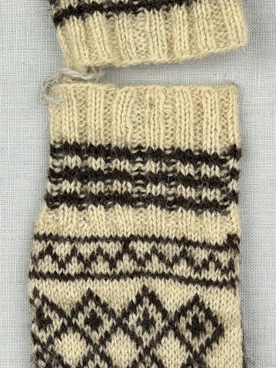 Ett par stickade fingervantar, med randig mudd i 2-2 resår (2 räta och 2 aviga maskor) och mönsterstickad vante i slätstickning, av 2-trådigt ullgarn.
