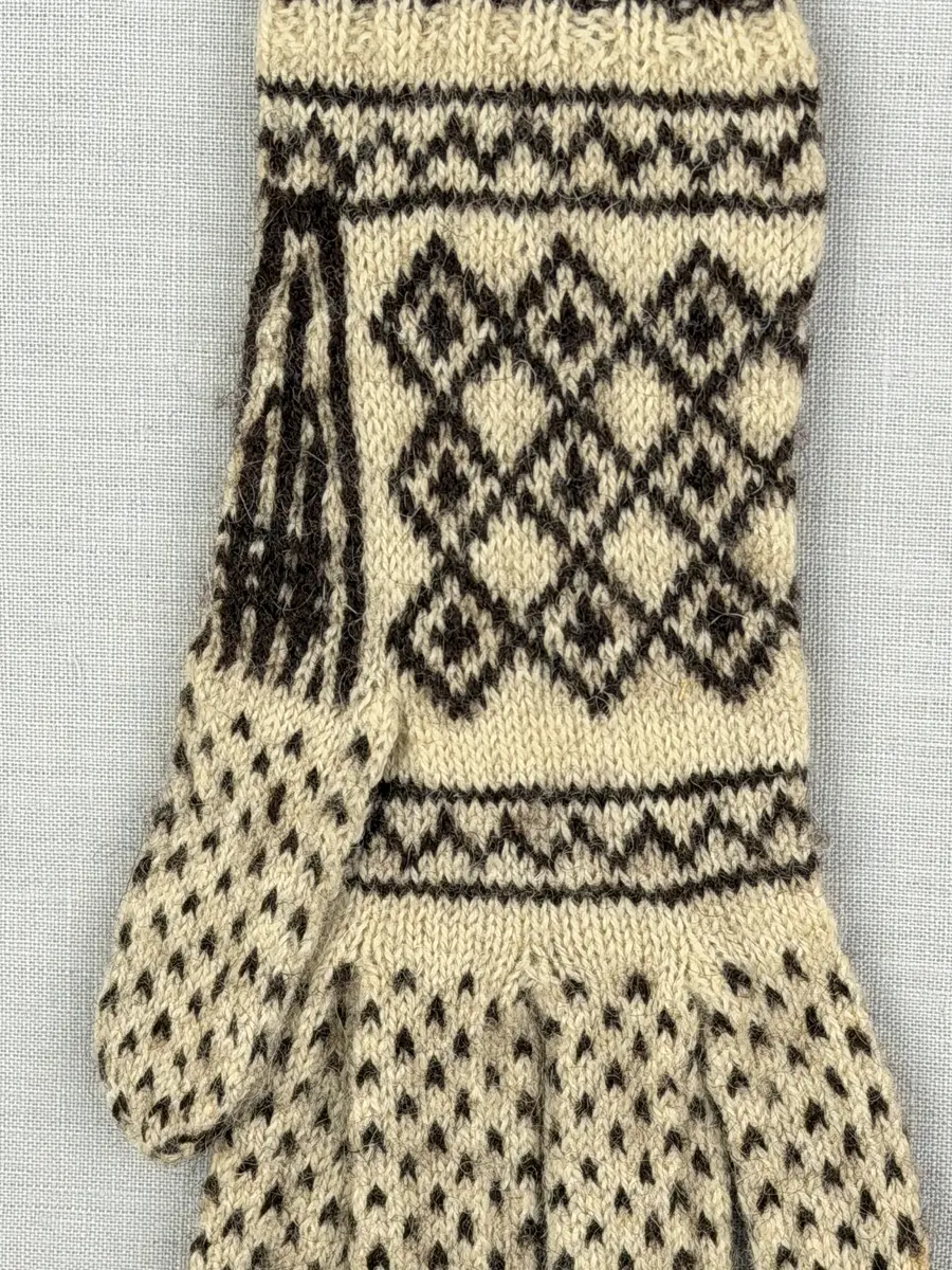 Ett par stickade fingervantar, med randig mudd i 2-2 resår (2 räta och 2 aviga maskor) och mönsterstickad vante i slätstickning, av 2-trådigt ullgarn.
