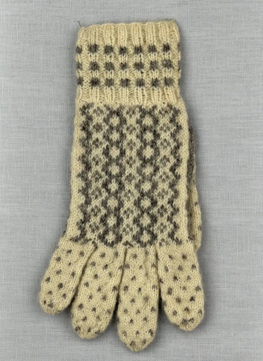 En stickad fingervante, med mönstrad mudd i 2-2 resår (2 räta och 2 aviga maskor) och mönsterstickad vante i slätstickning, av 2-trådigt ullgarn.
