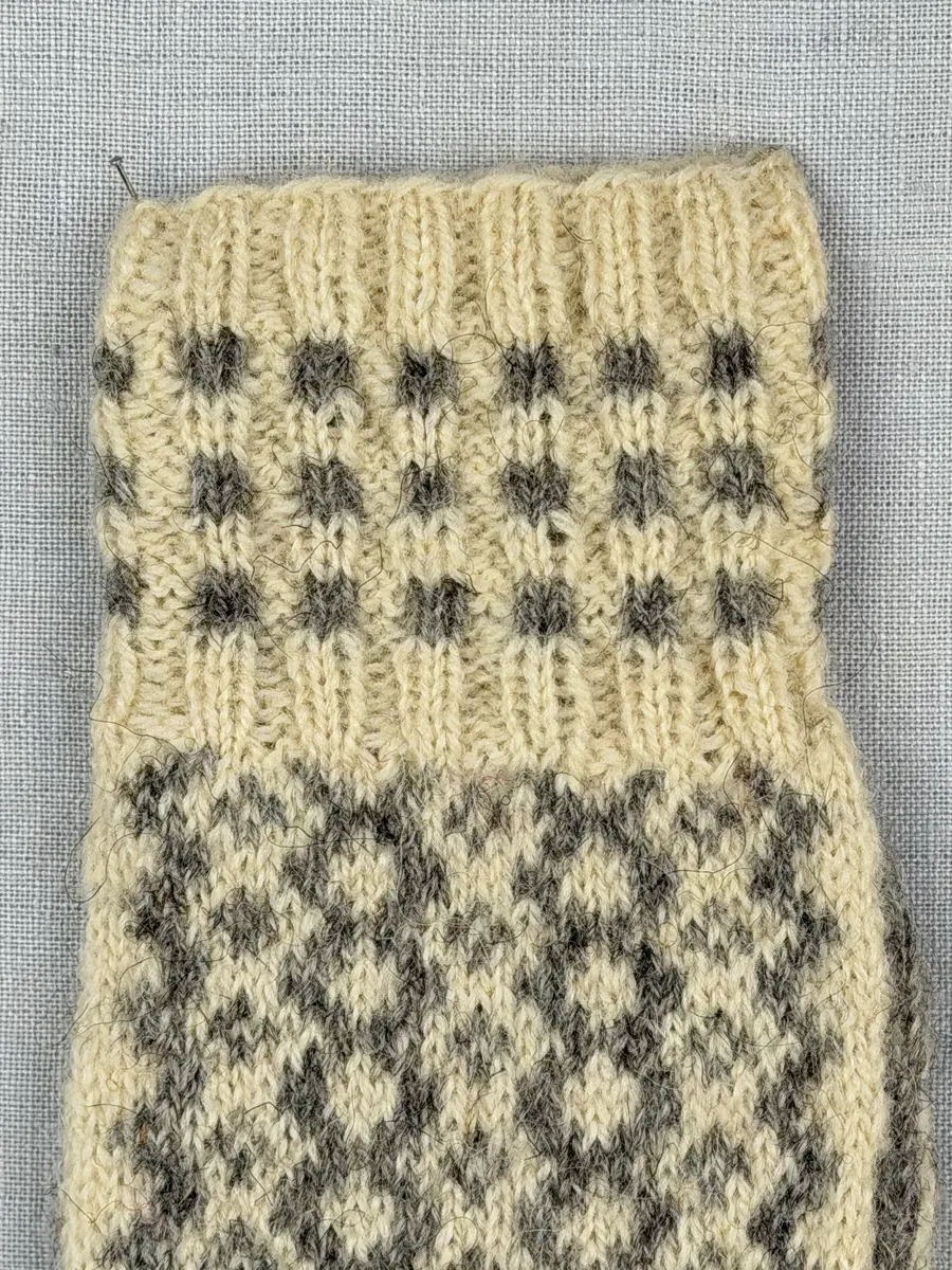 En stickad fingervante, med mönstrad mudd i 2-2 resår (2 räta och 2 aviga maskor) och mönsterstickad vante i slätstickning, av 2-trådigt ullgarn.