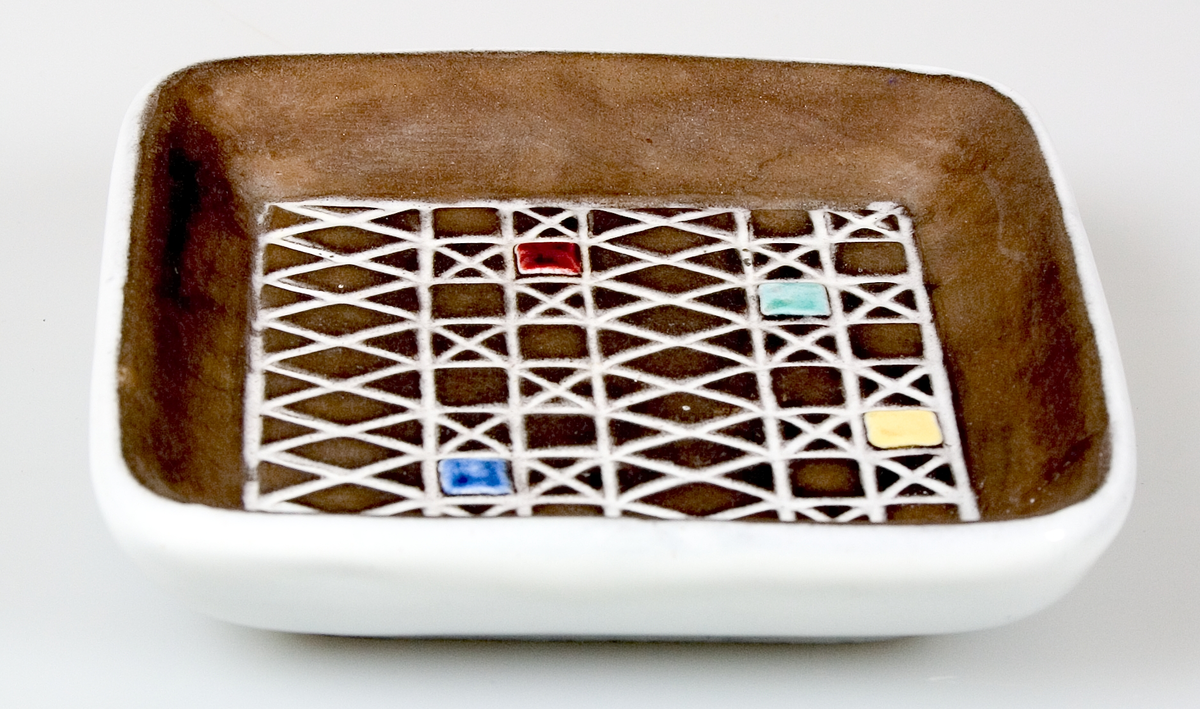 Fyrkantigt fat med rundade hörn. Vit glasyr på undersidan. Geometrisk ristad dekor på ovansidan. Dekoren glaserad i vitt, gult, rött, grönt och blått. I övrigt oglaserad (brungrå). Stämplad: 21 44 UE Abg