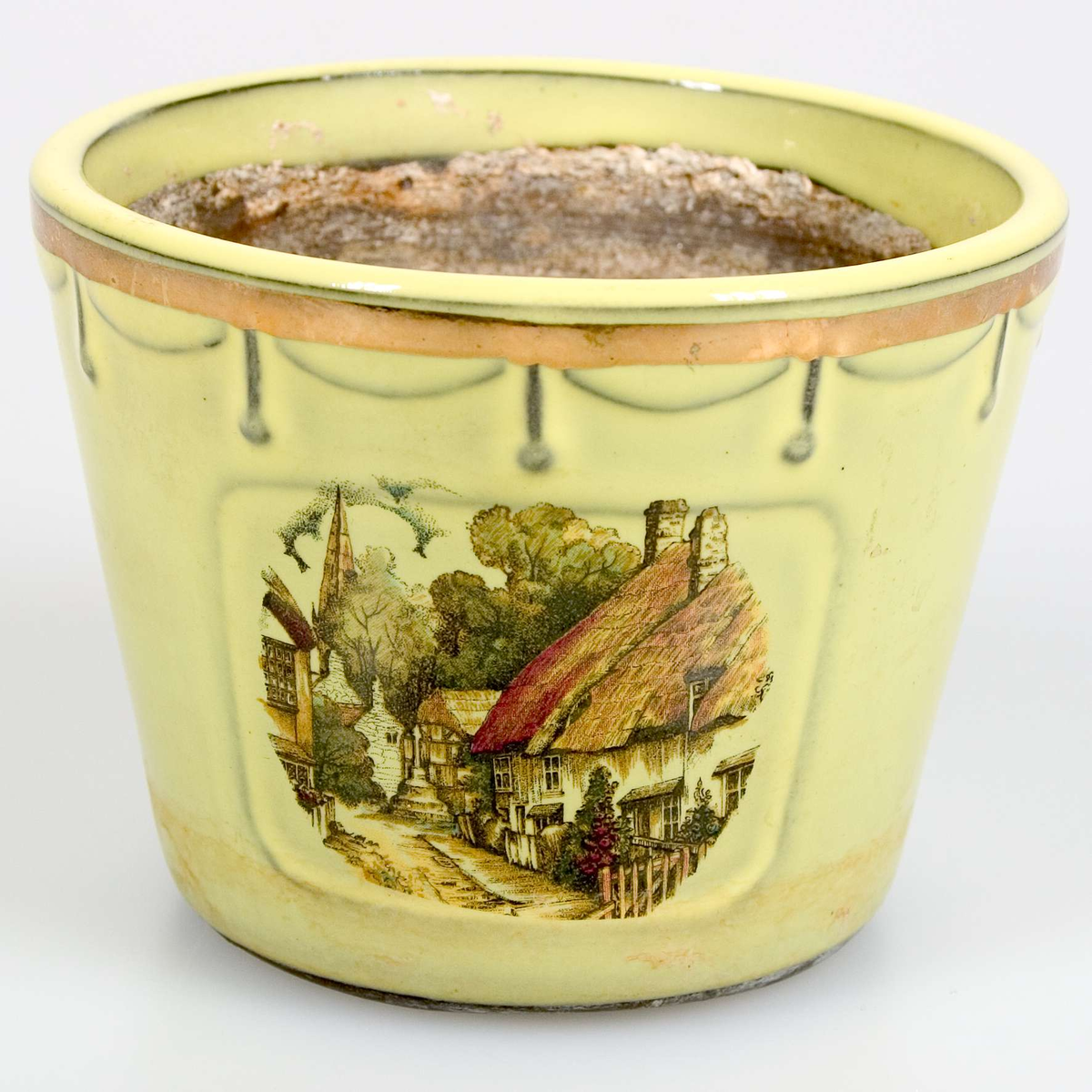 Cylinderformad kruka med något utåtlutande väggar. Gulglaserade på utsidan, med en förgylld reliefbård runt överkanten. På sidorna två tryckta fyrkanter, med motiv av korsvirkeshus, i flera färger. Oglaserad på insidan, runt hål i botten. Stämplad Ekeby, Sweden 1