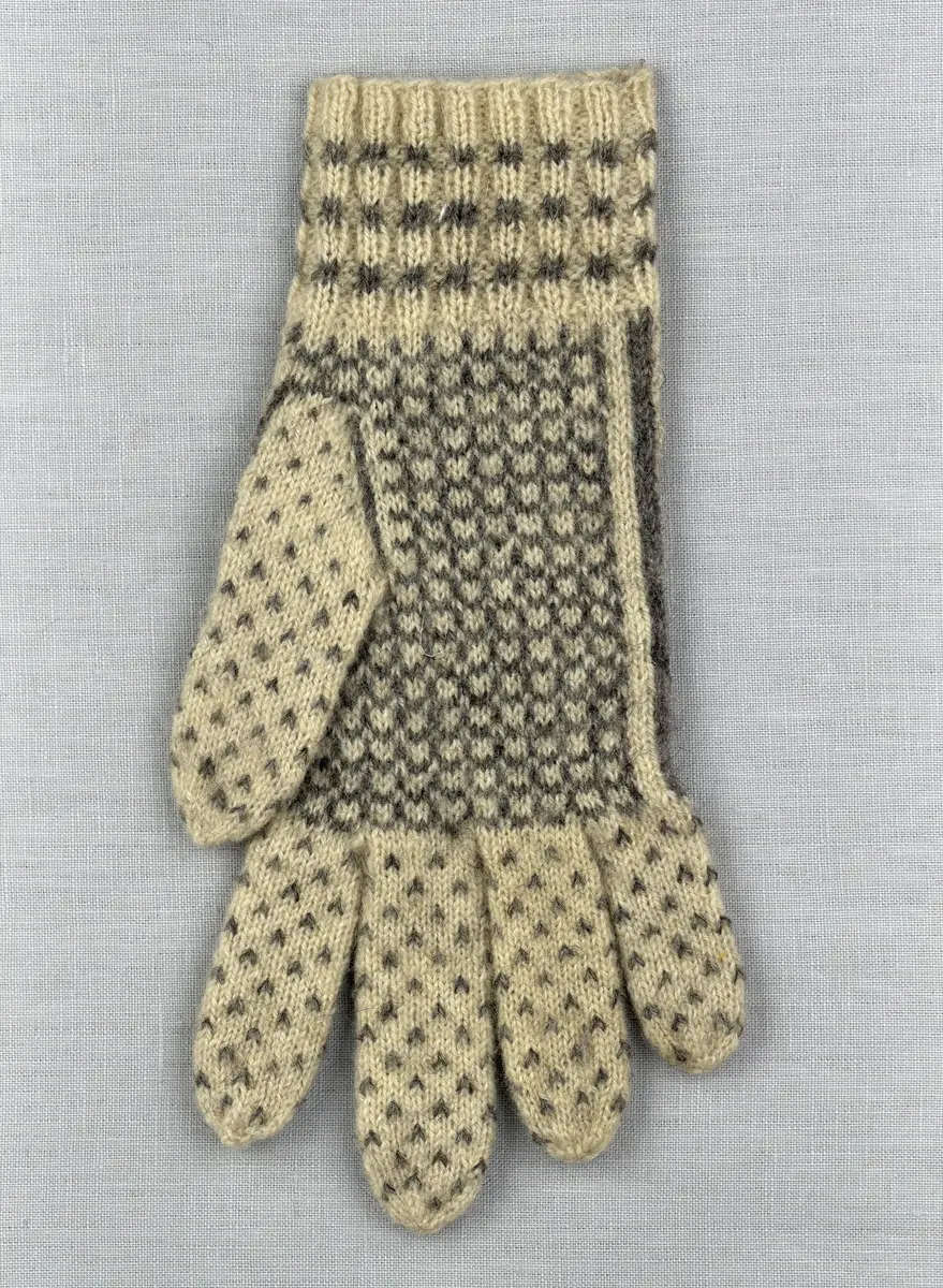 En stickad fingervante, med mönstrad mudd i 2-2 resår (2 räta och 2 aviga maskor) och mönsterstickad vante i slätstickning, av 2-trådigt ullgarn.