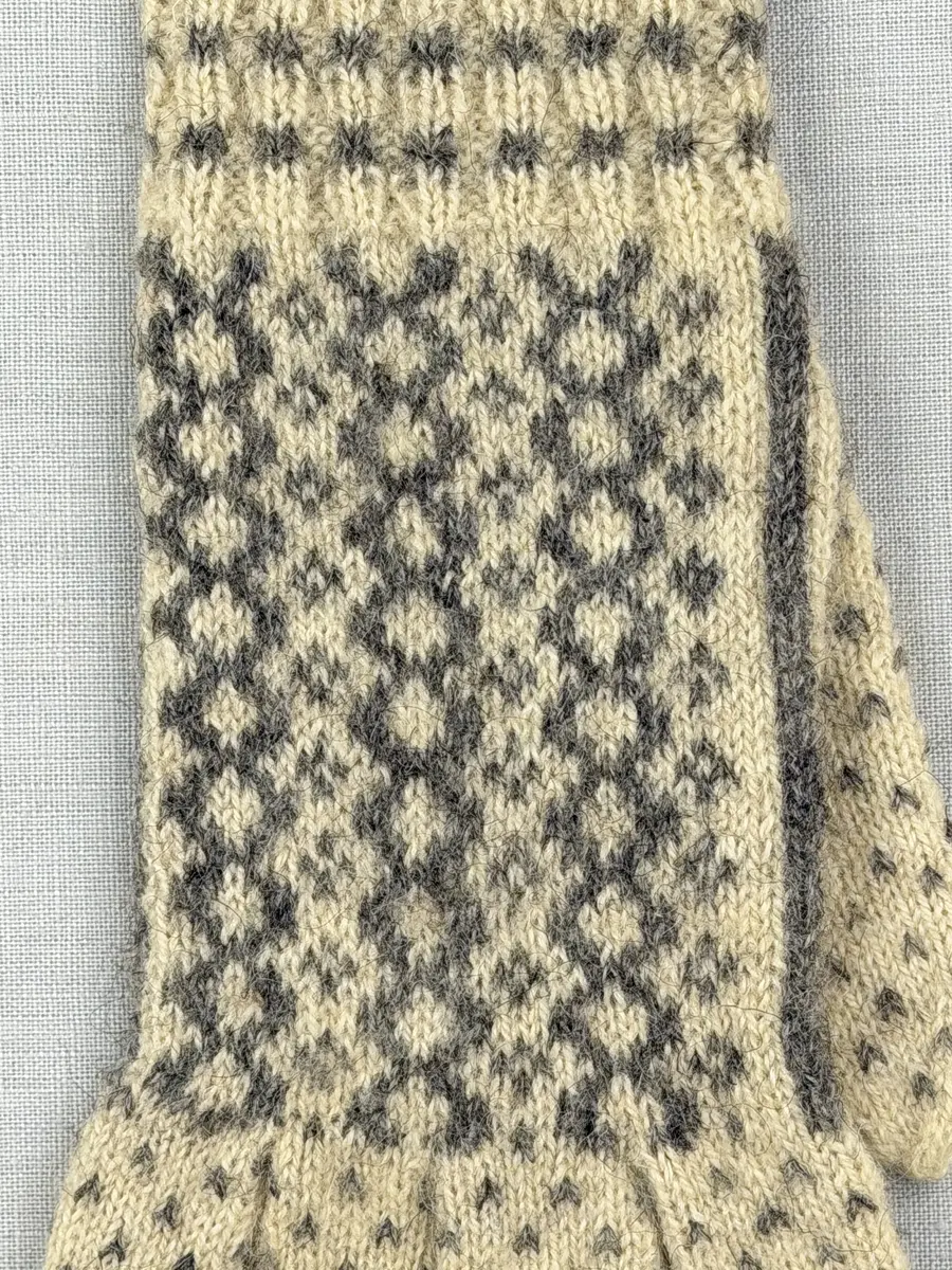 En stickad fingervante, med mönstrad mudd i 2-2 resår (2 räta och 2 aviga maskor) och mönsterstickad vante i slätstickning, av 2-trådigt ullgarn.