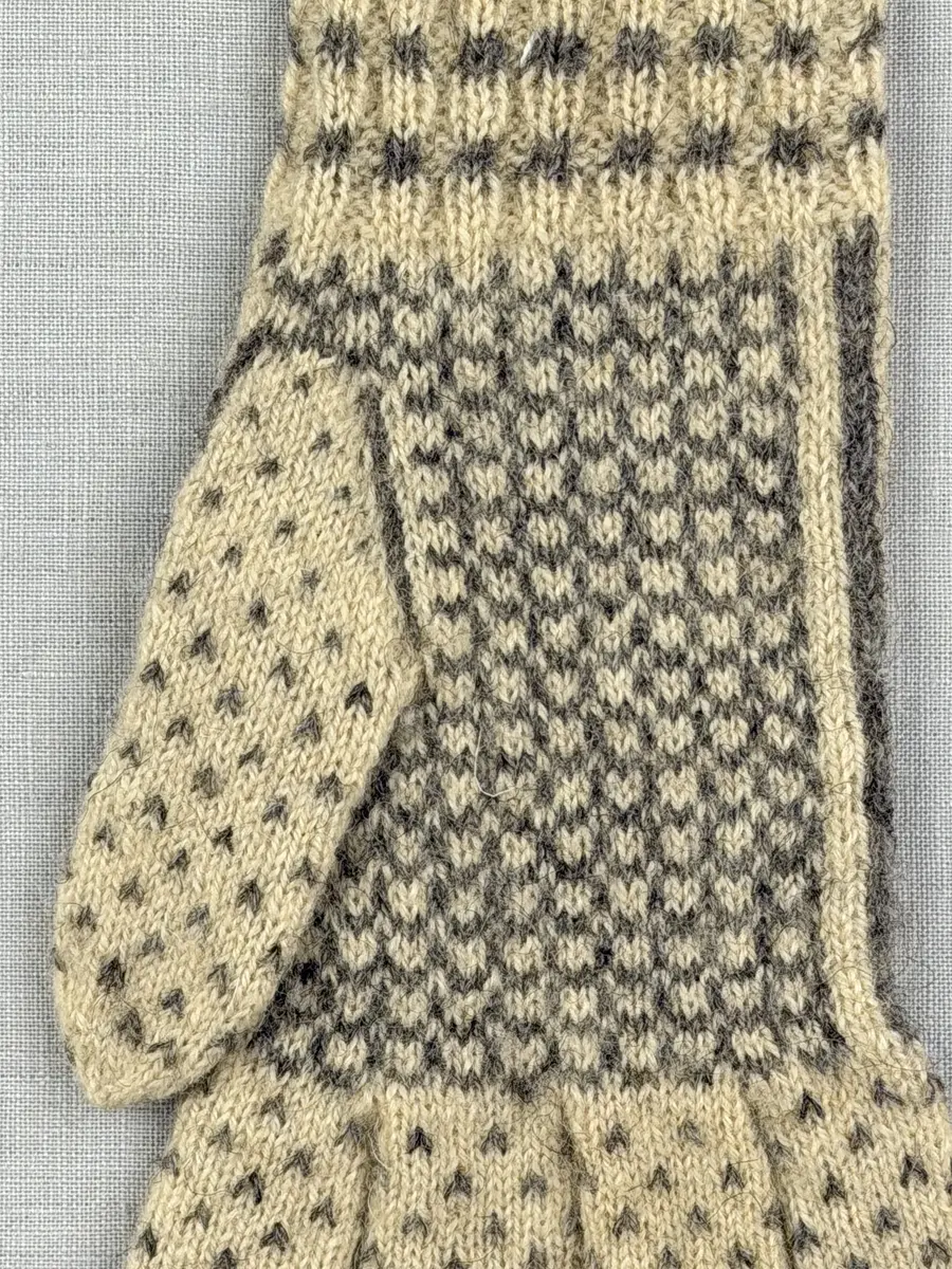 En stickad fingervante, med mönstrad mudd i 2-2 resår (2 räta och 2 aviga maskor) och mönsterstickad vante i slätstickning, av 2-trådigt ullgarn.