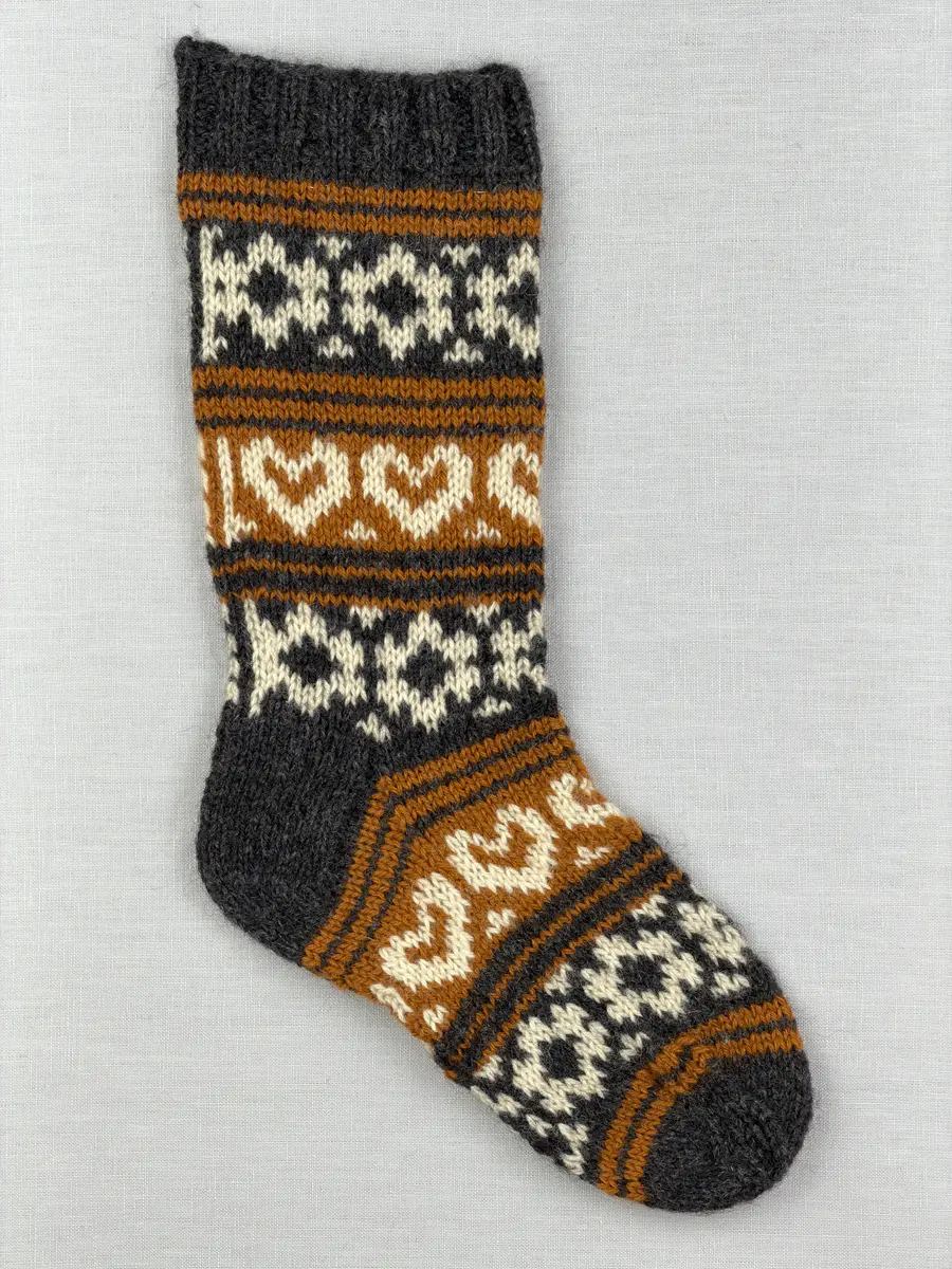 En stickad socka, med mudd i 2-2 resår (2 räta och2 aviga maskor) samt mönsterstickad fot och skaft i slätstickning, av 3-trådigt ullgarn.