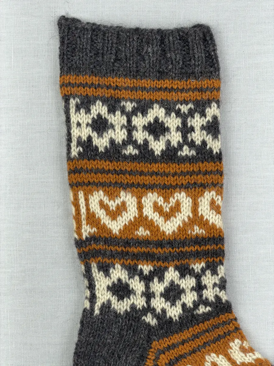 En stickad socka, med mudd i 2-2 resår (2 räta och2 aviga maskor) samt mönsterstickad fot och skaft i slätstickning, av 3-trådigt ullgarn.