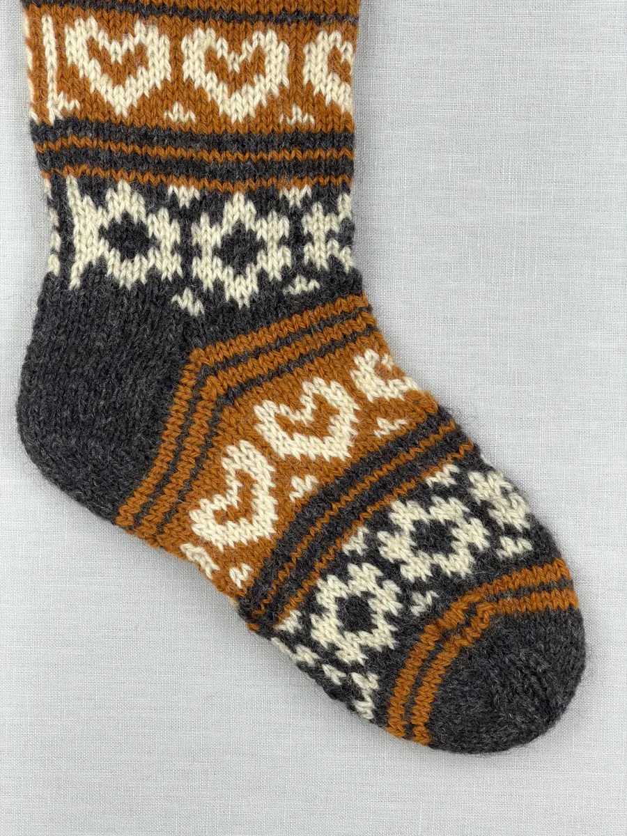 En stickad socka, med mudd i 2-2 resår (2 räta och2 aviga maskor) samt mönsterstickad fot och skaft i slätstickning, av 3-trådigt ullgarn.