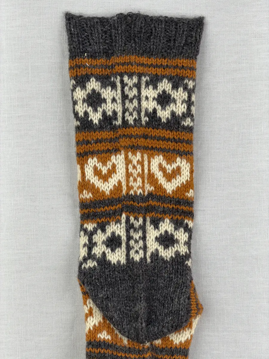 En stickad socka, med mudd i 2-2 resår (2 räta och2 aviga maskor) samt mönsterstickad fot och skaft i slätstickning, av 3-trådigt ullgarn.