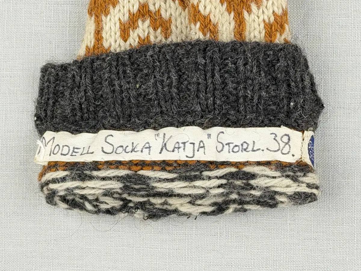 En stickad socka, med mudd i 2-2 resår (2 räta och2 aviga maskor) samt mönsterstickad fot och skaft i slätstickning, av 3-trådigt ullgarn.