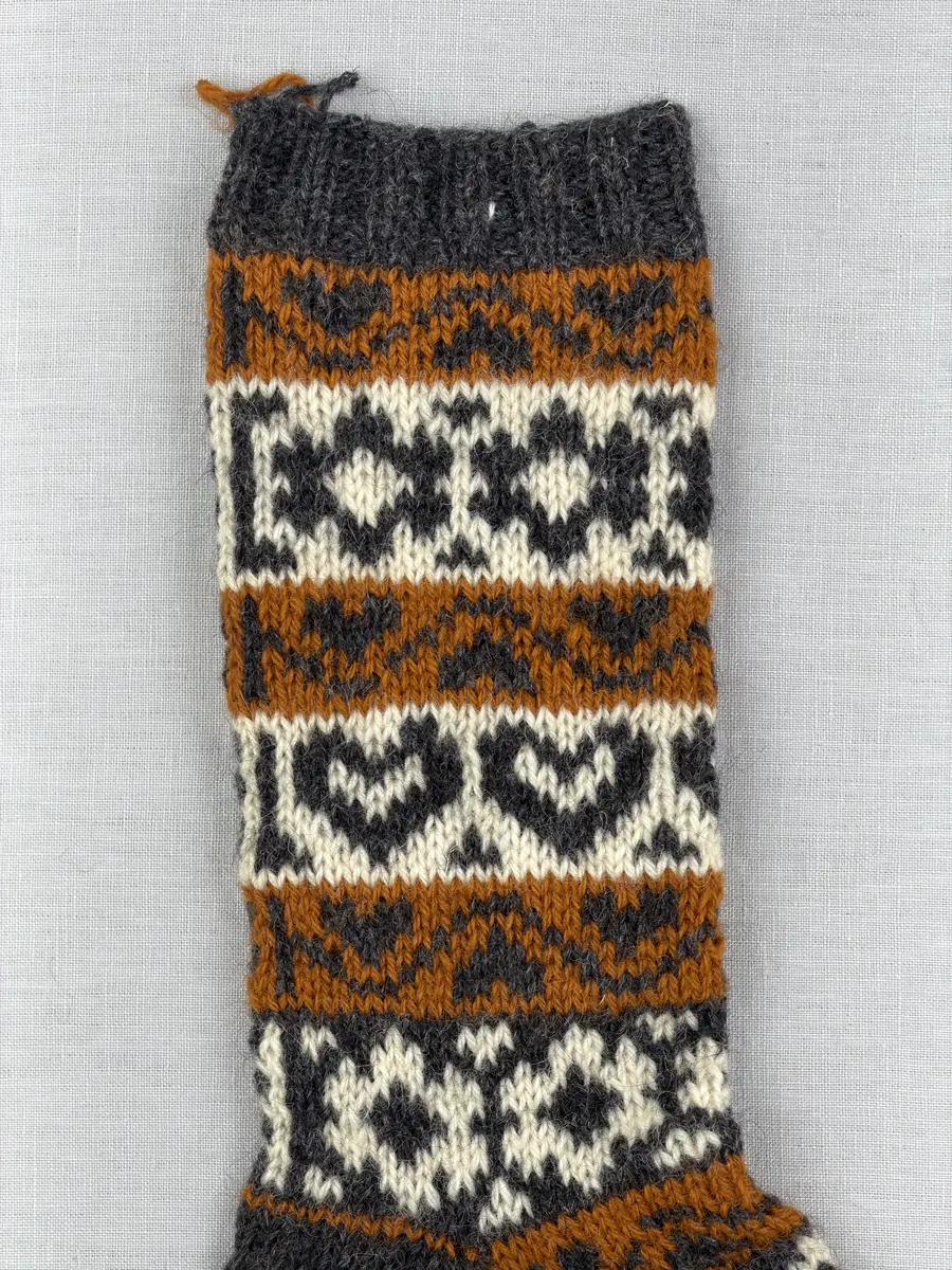 En stickad socka, med mudd i 2-2 resår (2 räta och2 aviga maskor) samt mönsterstickad fot och skaft i slätstickning, av 3-trådigt ullgarn.