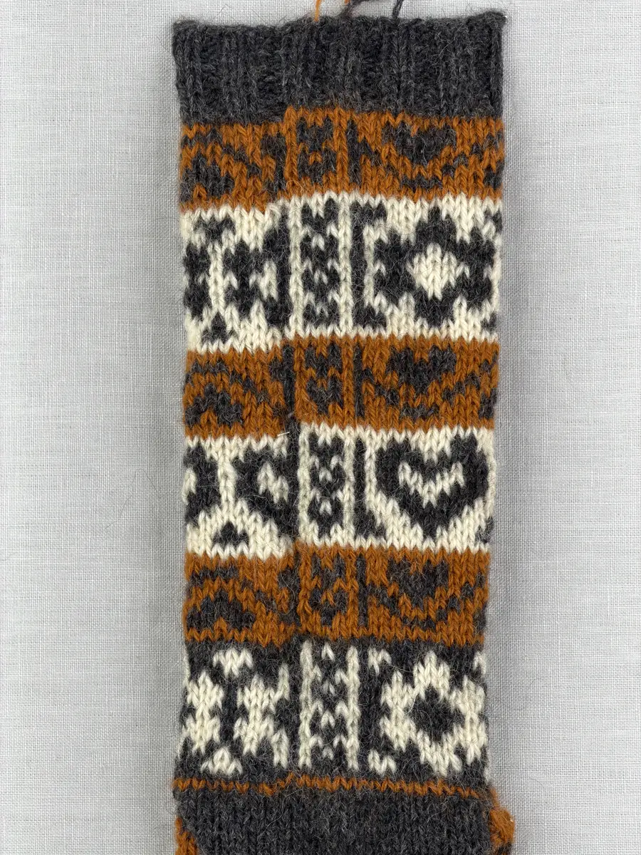 En stickad socka, med mudd i 2-2 resår (2 räta och2 aviga maskor) samt mönsterstickad fot och skaft i slätstickning, av 3-trådigt ullgarn.