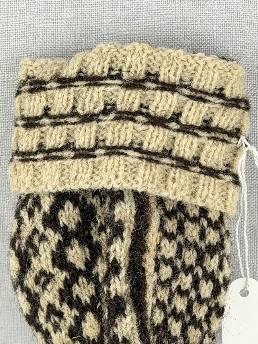 En stickad fingervante, med mönstrad mudd i 2-2 resår (2 räta och 2 aviga maskor) och mönsterstickad vante i slätstickning, av 2-trådigt ullgarn.