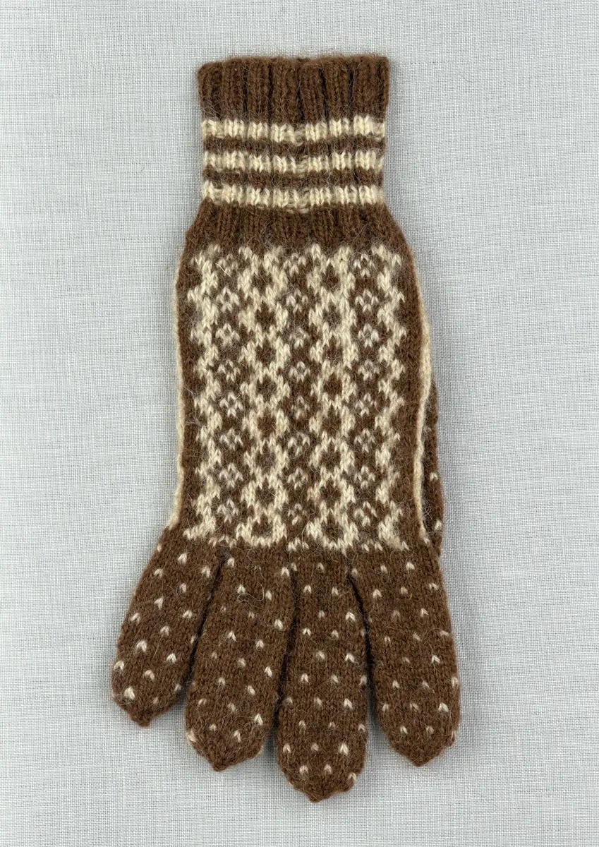 En stickad fingervante, med mönstrad mudd i 2-2 resår (2 räta och 2 aviga maskor) och mönsterstickad vante i slätstickning, av 2-trådigt ullgarn.