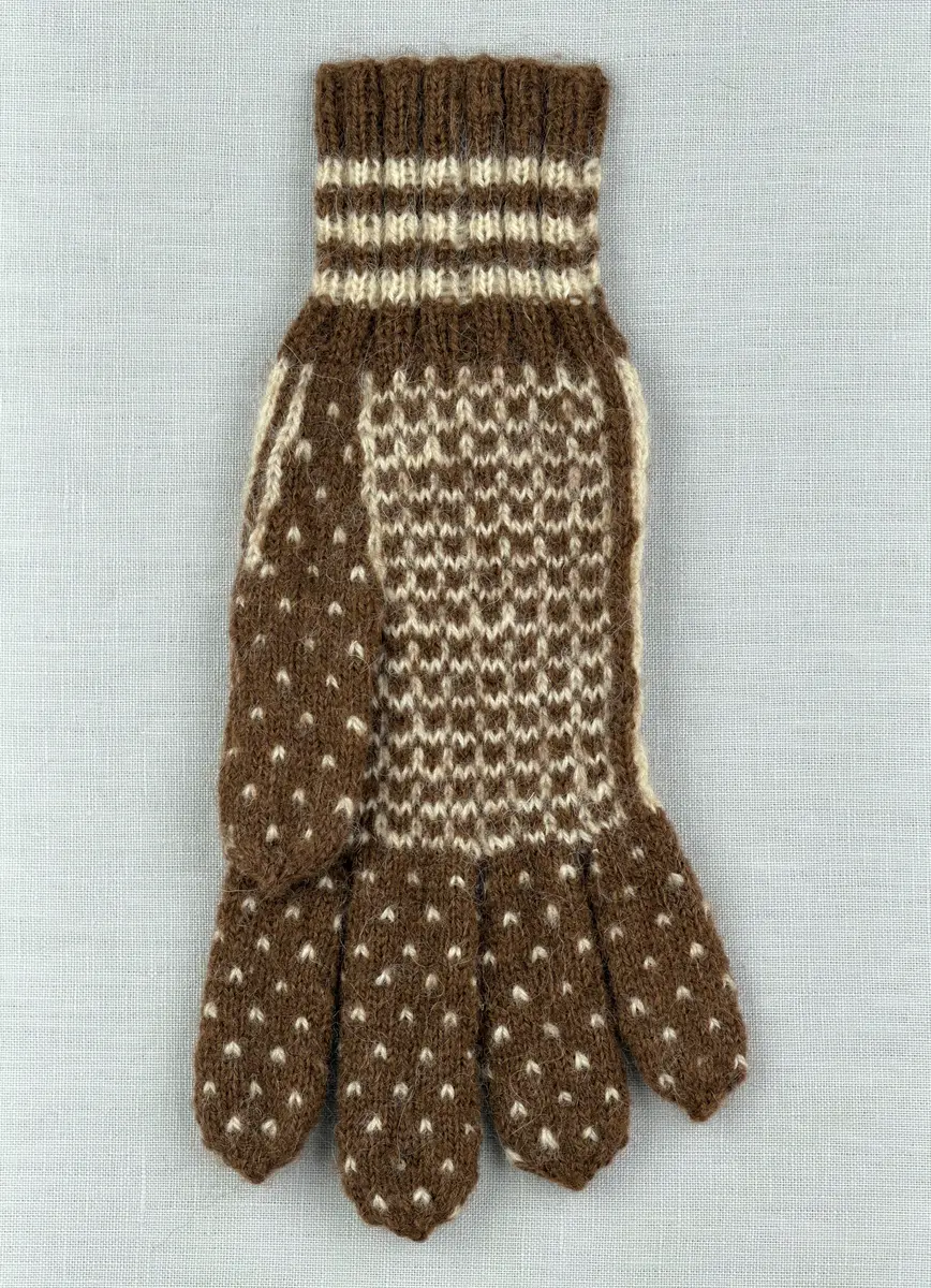 En stickad fingervante, med mönstrad mudd i 2-2 resår (2 räta och 2 aviga maskor) och mönsterstickad vante i slätstickning, av 2-trådigt ullgarn.