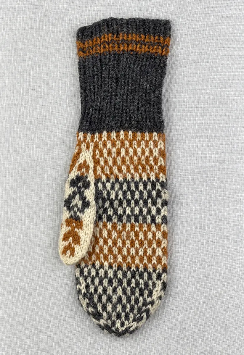 En stickad tumvante, med randig mudd i 1-1 resår (1 rät och 1 avig maska) och mönsterstickad vante i slätstickning, av 3-trådigt ullgarn.